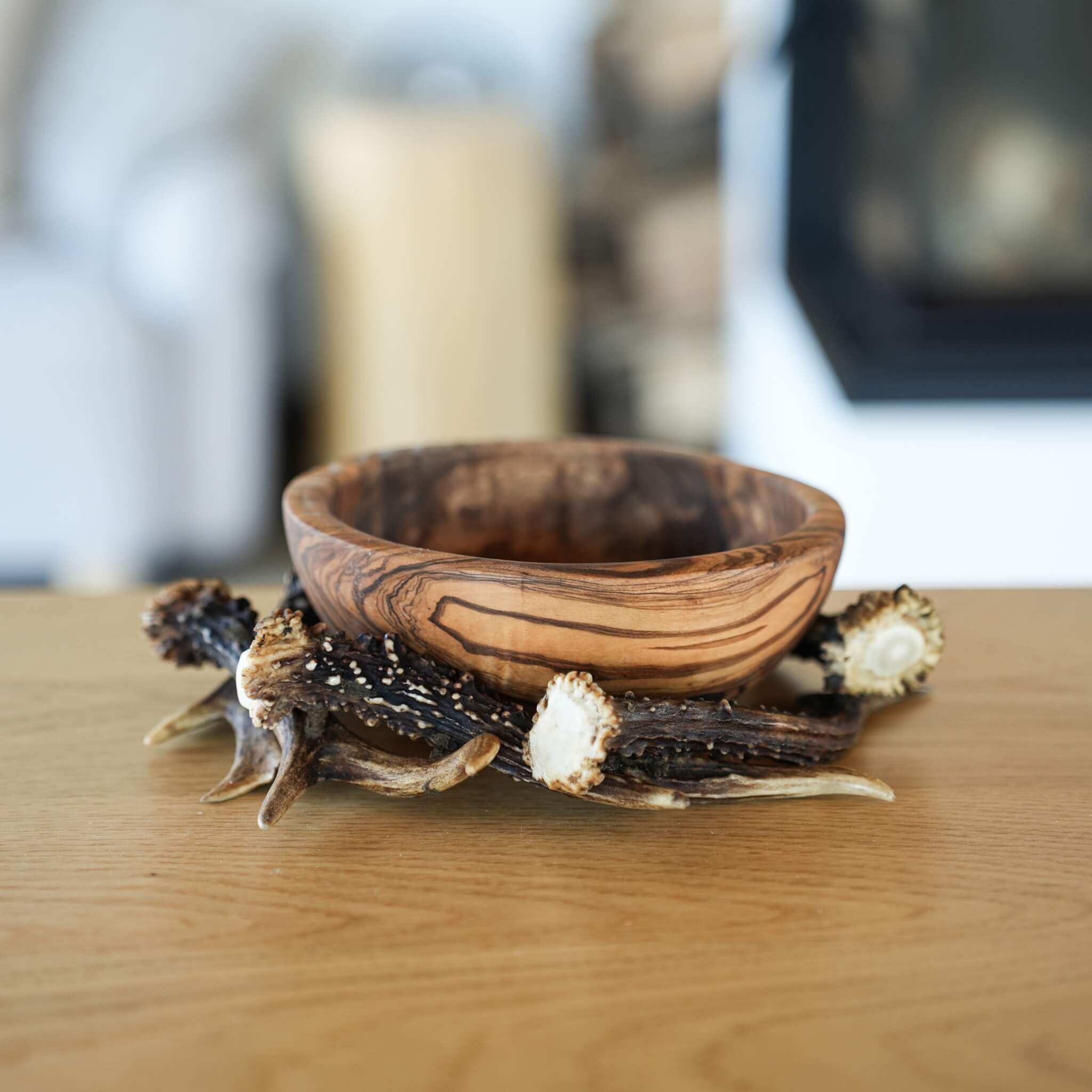 Decorative olive wood bowl resting in a natural antler ring, with a light wood background.