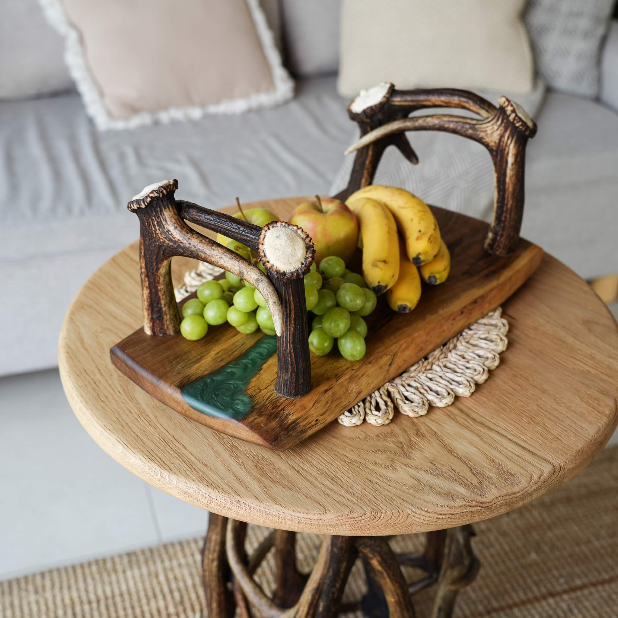 Olive wood tray with antler handles and green epoxy inlay, filled with fresh fruit, displayed on a rustic antler-leg table.
